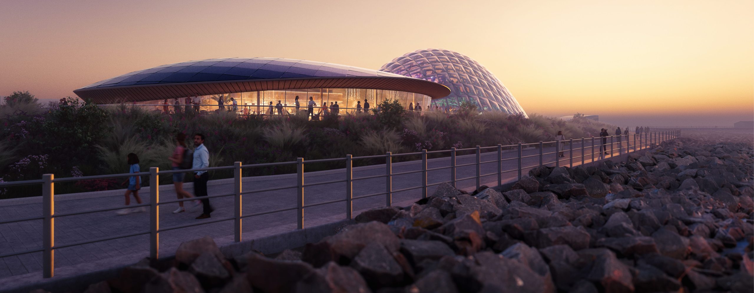 Modern architectural design of the Eden Project in Morecambe, featuring a glass dome and a curved building, with people walking along a pathway at sunset.