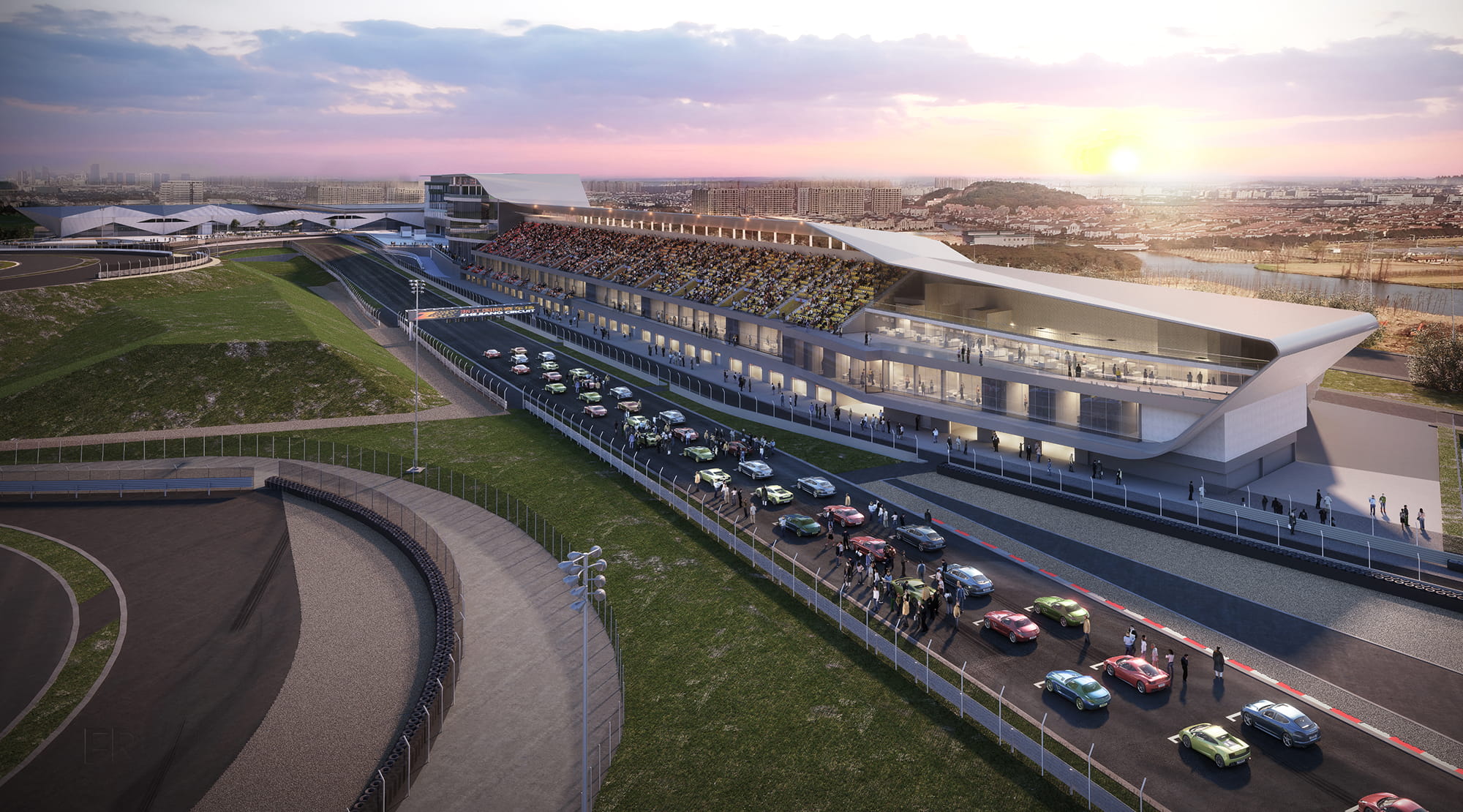 Aerial view of a modern motorsport racetrack with a grandstand filled with spectators, cars lined up on the track, and a sunset in the background.