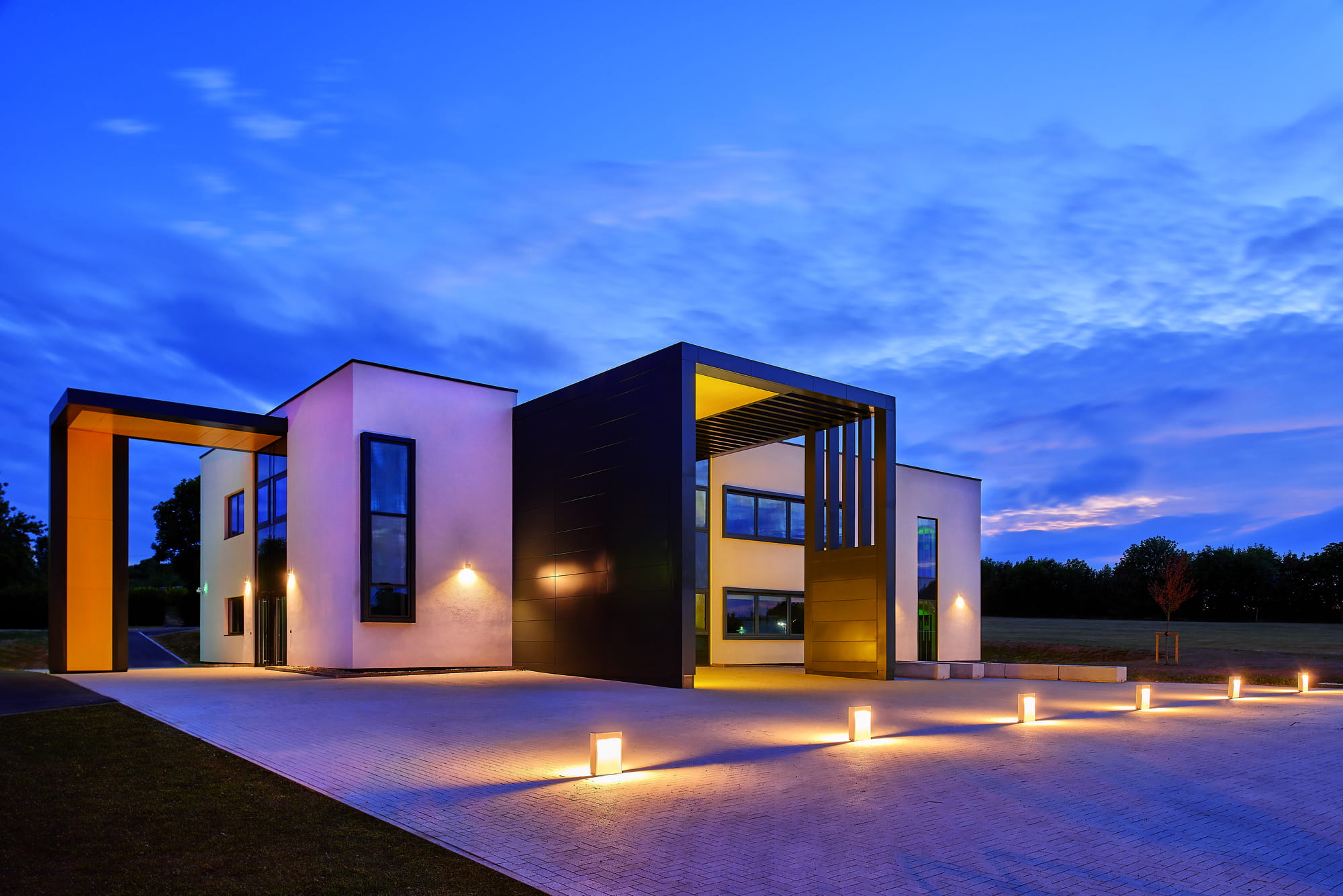 Modern school building with large windows and a distinctive entrance, illuminated at dusk.