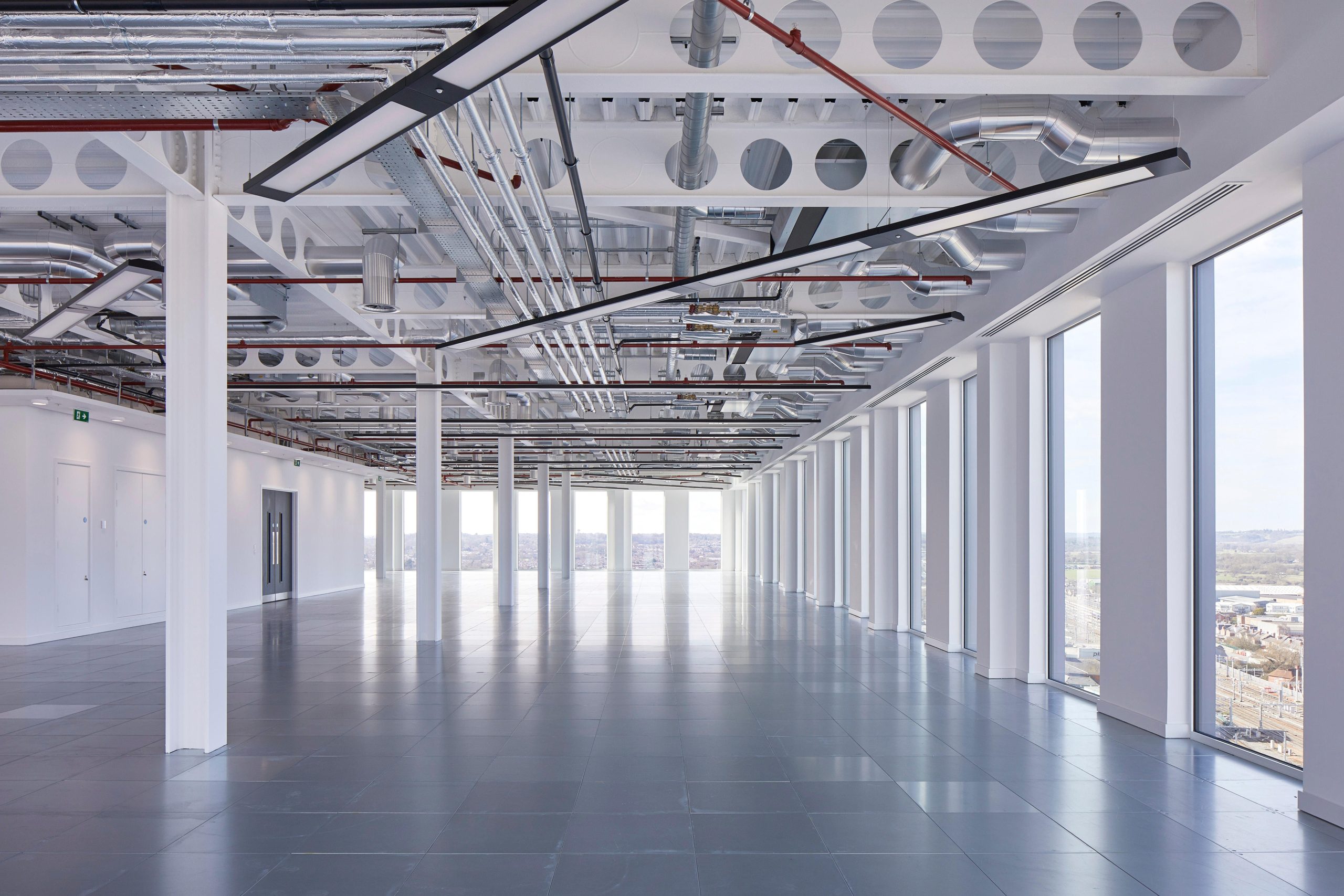 Spacious, modern office interior featuring large windows, polished flooring, and exposed ceiling infrastructure.