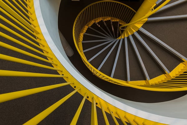 Spiral staircase with yellow railings and gray steps, viewed from above.