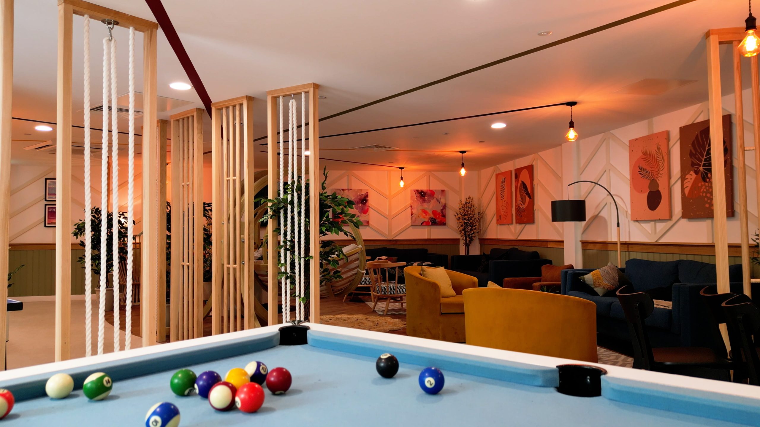 A pool table with colorful balls in a modern lounge area featuring plants, artwork on the walls, and cozy seating arrangements.