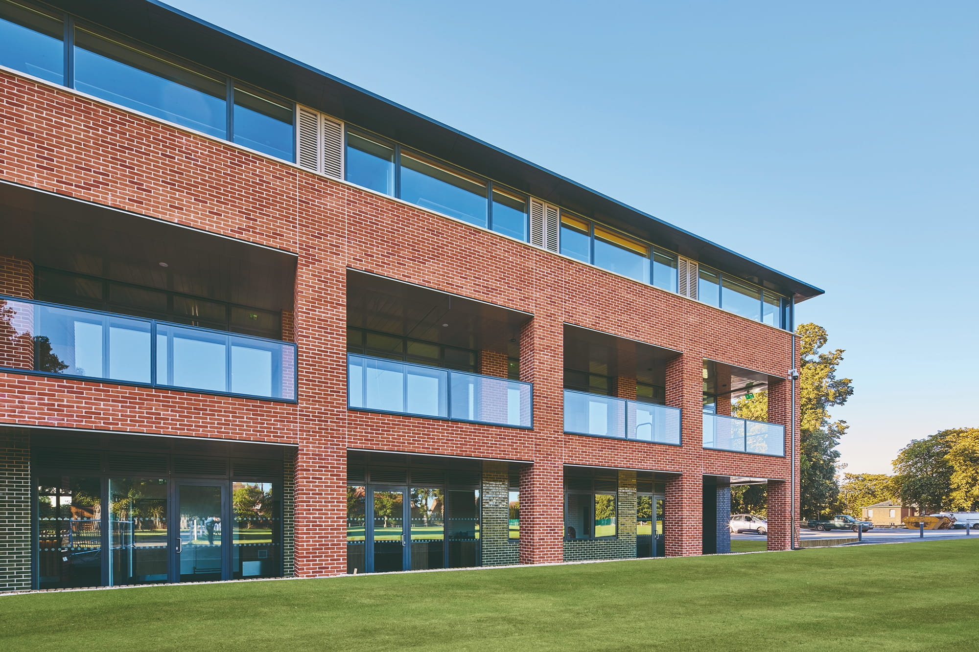 Modern brick building with large windows and balconies, set against a clear blue sky and green lawn.