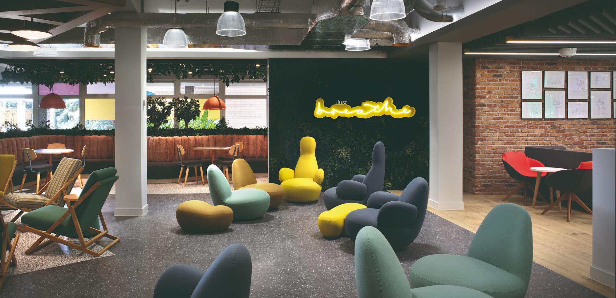 Colorful seating arrangements in a modern lounge area with a neon sign that reads "just breathe" and a brick wall featuring framed artwork.