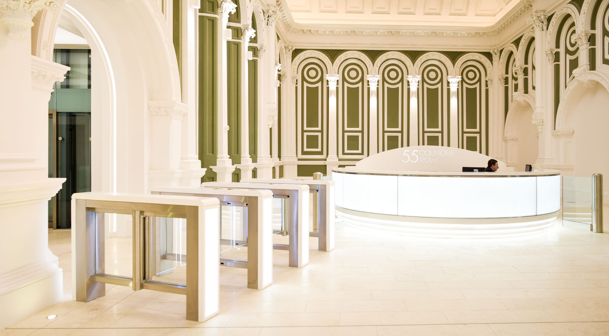 Reception area of a commercial building featuring a curved front desk, modern turnstiles, and ornate architectural details in green and white.