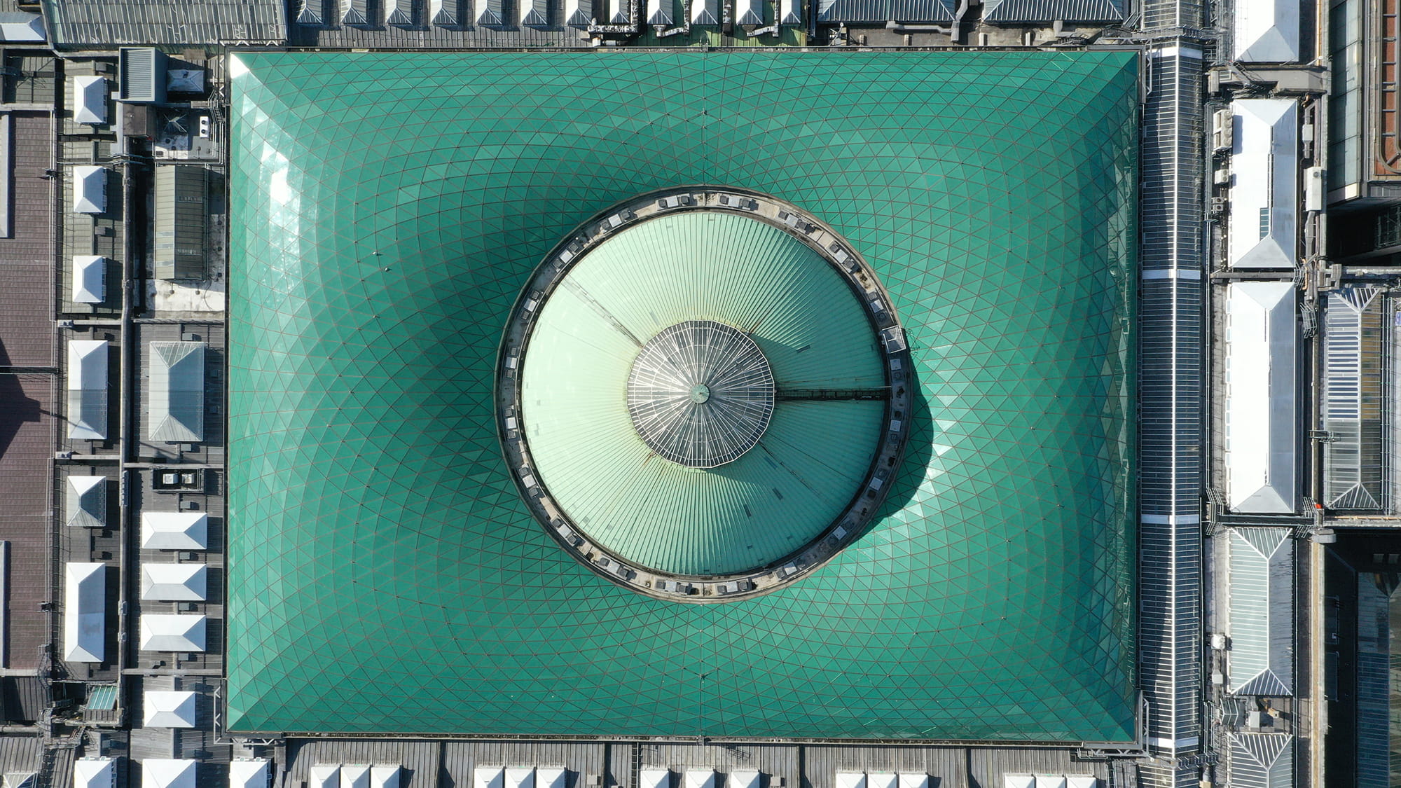 Aerial view of a large green dome with a geometric pattern, surrounded by smaller white structures.