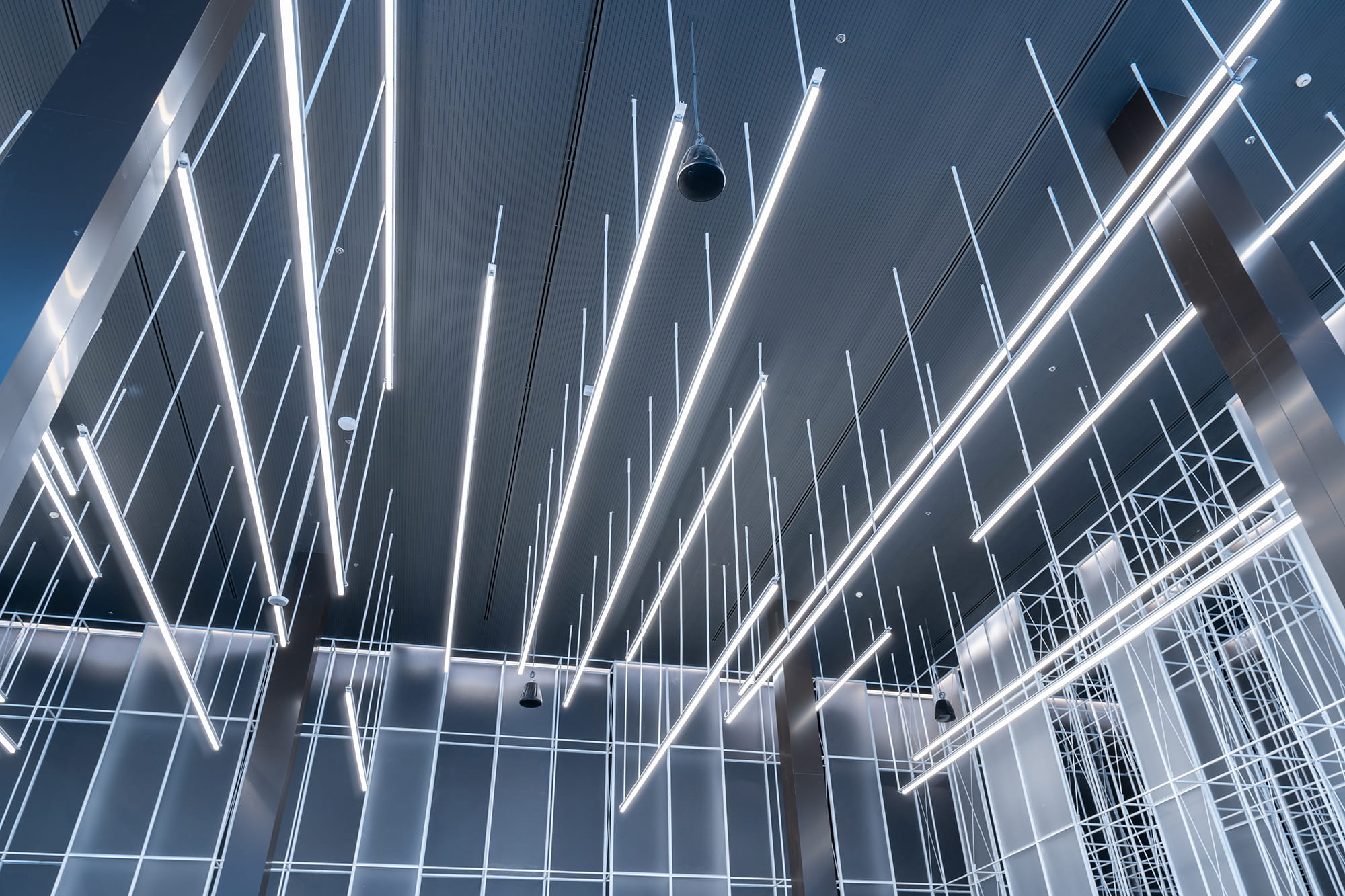 Modern ceiling design featuring linear LED light fixtures suspended at various angles against a dark ceiling.