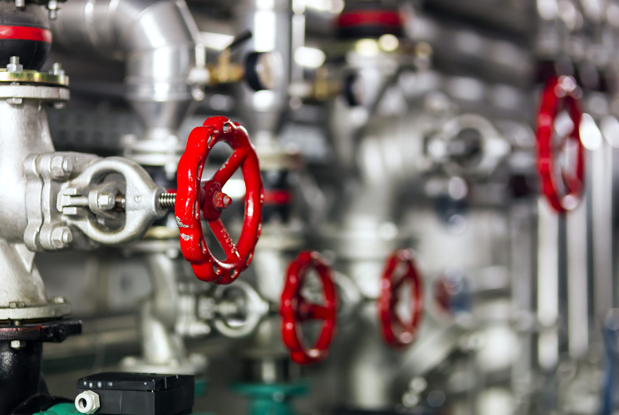 Close-up of industrial valves with red handles on a metallic piping system.
