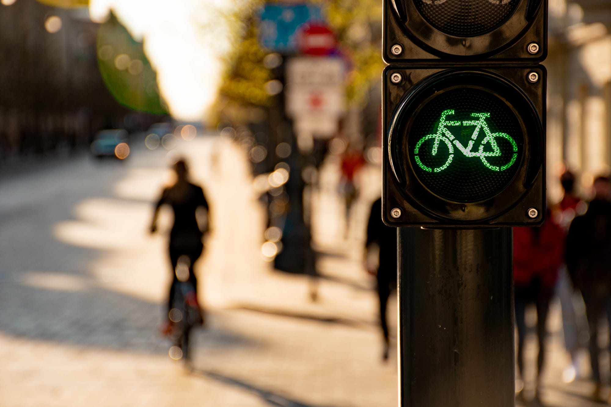 Green bicycle traffic signal with a blurred street and cyclists in the background.