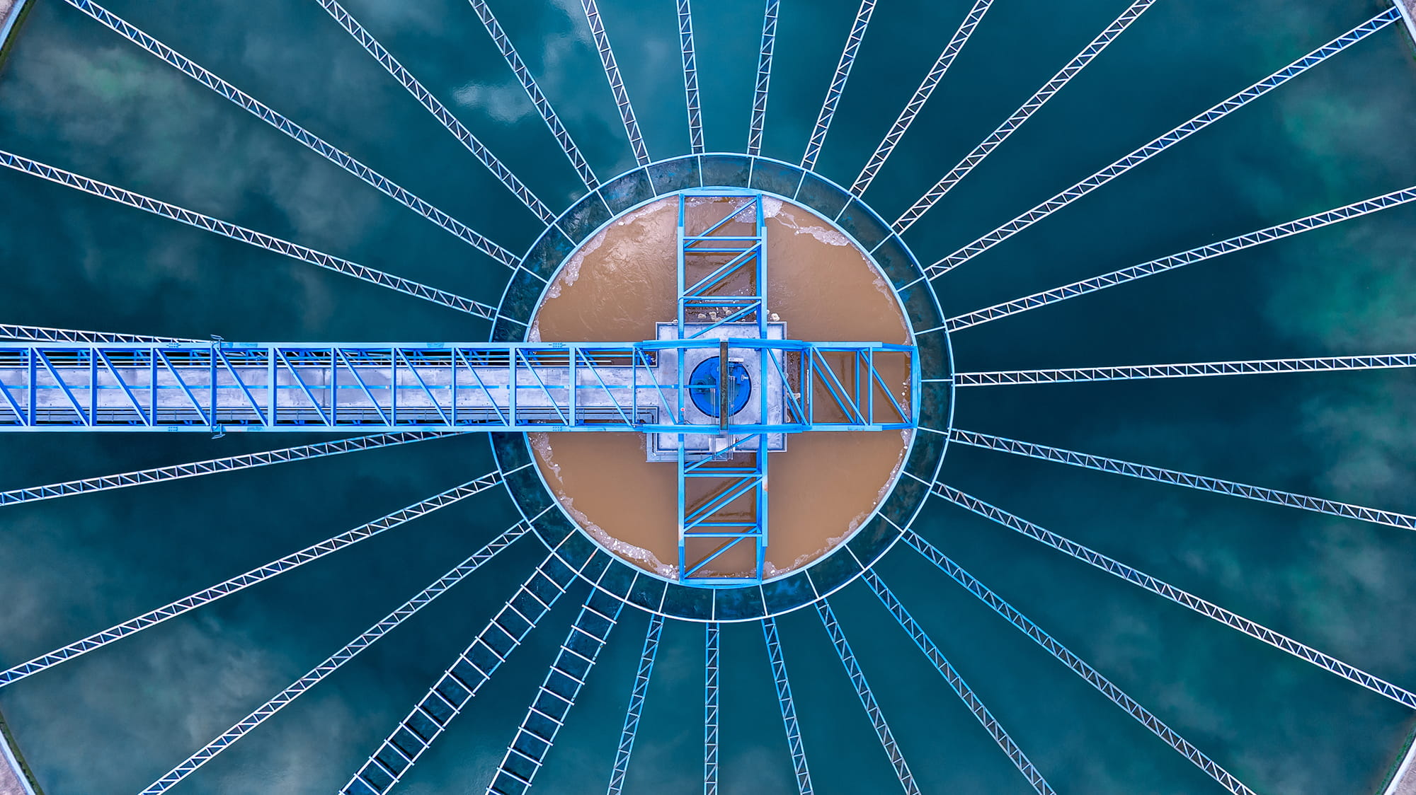 Aerial view of a circular water treatment facility with a central platform and radiating metal structures.