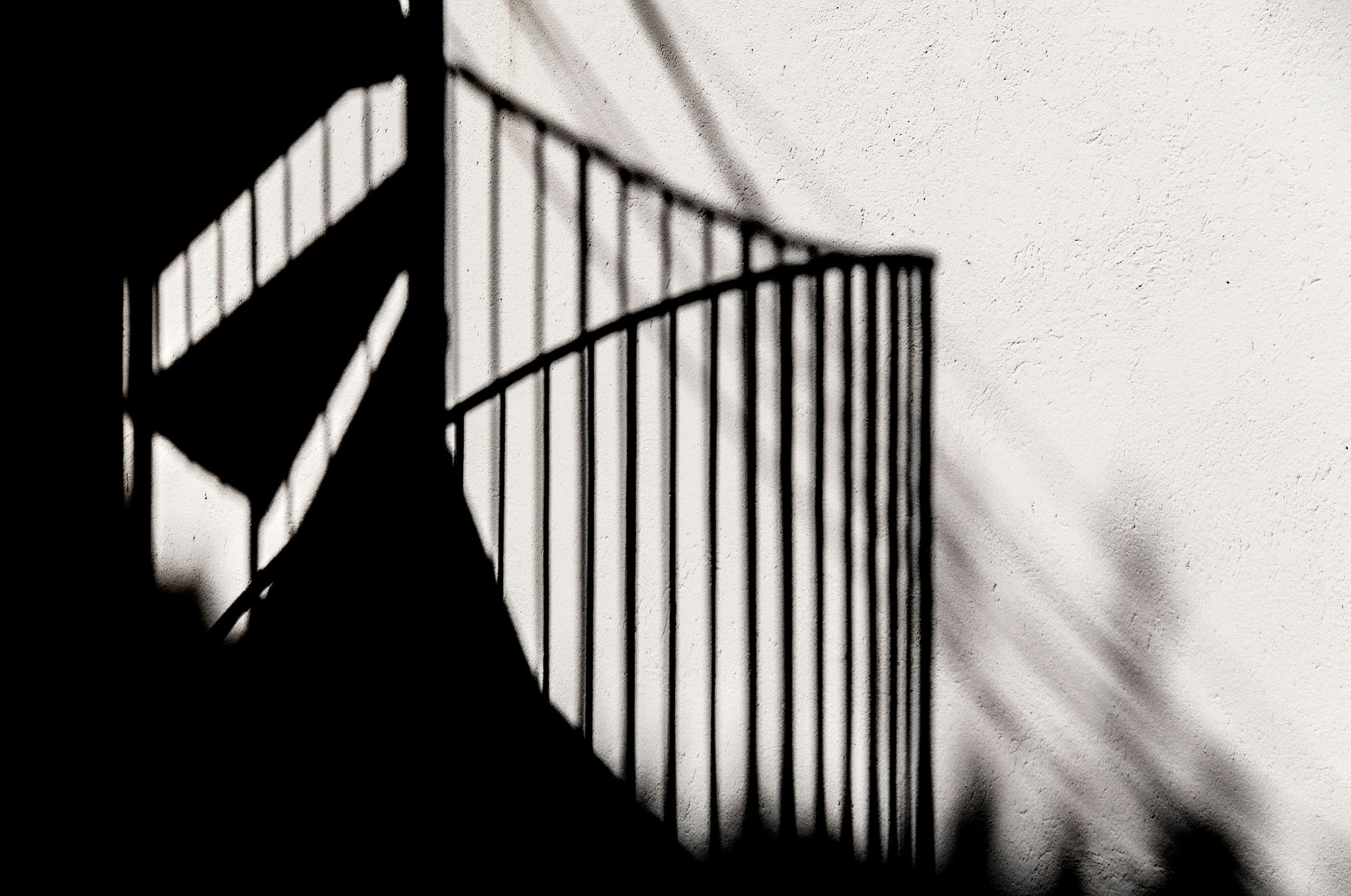 Shadow of a spiral staircase cast on a textured white wall.