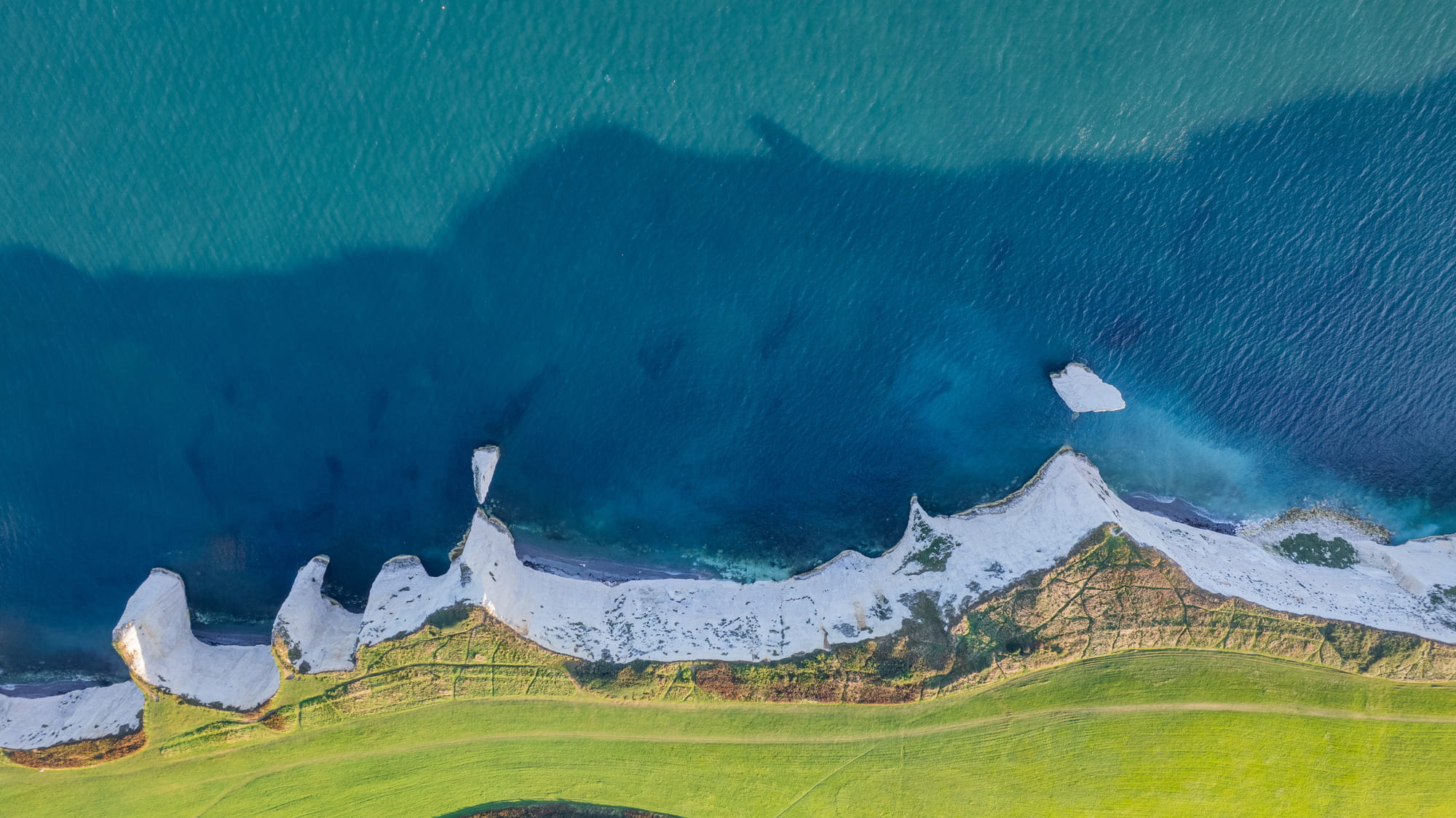 Aerial view of a coastline featuring white cliffs, green fields, and blue ocean water.