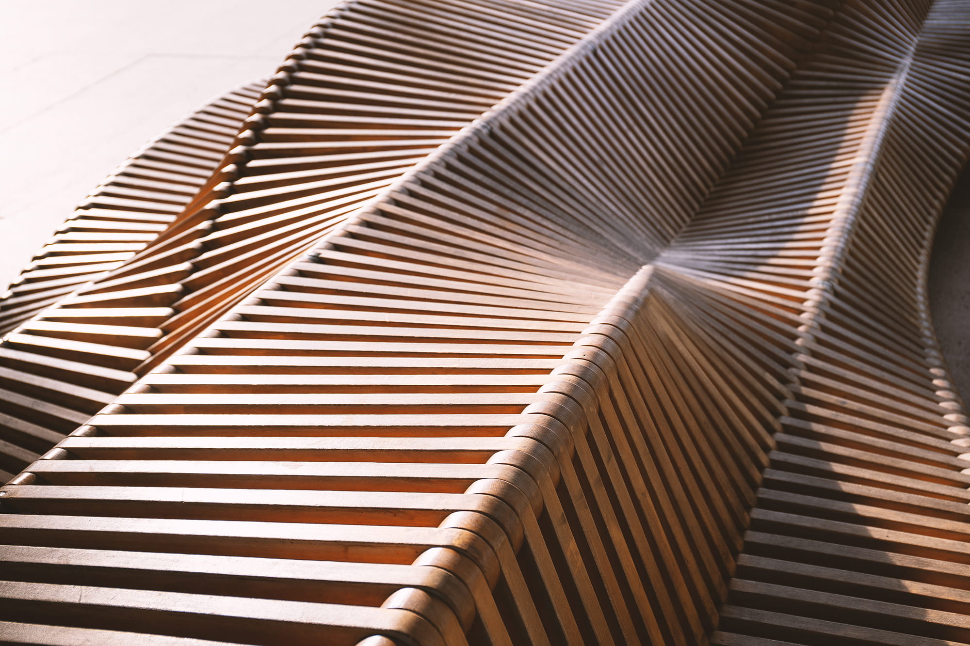 Curved wooden slats arranged in a wave pattern, creating a modern seating structure.