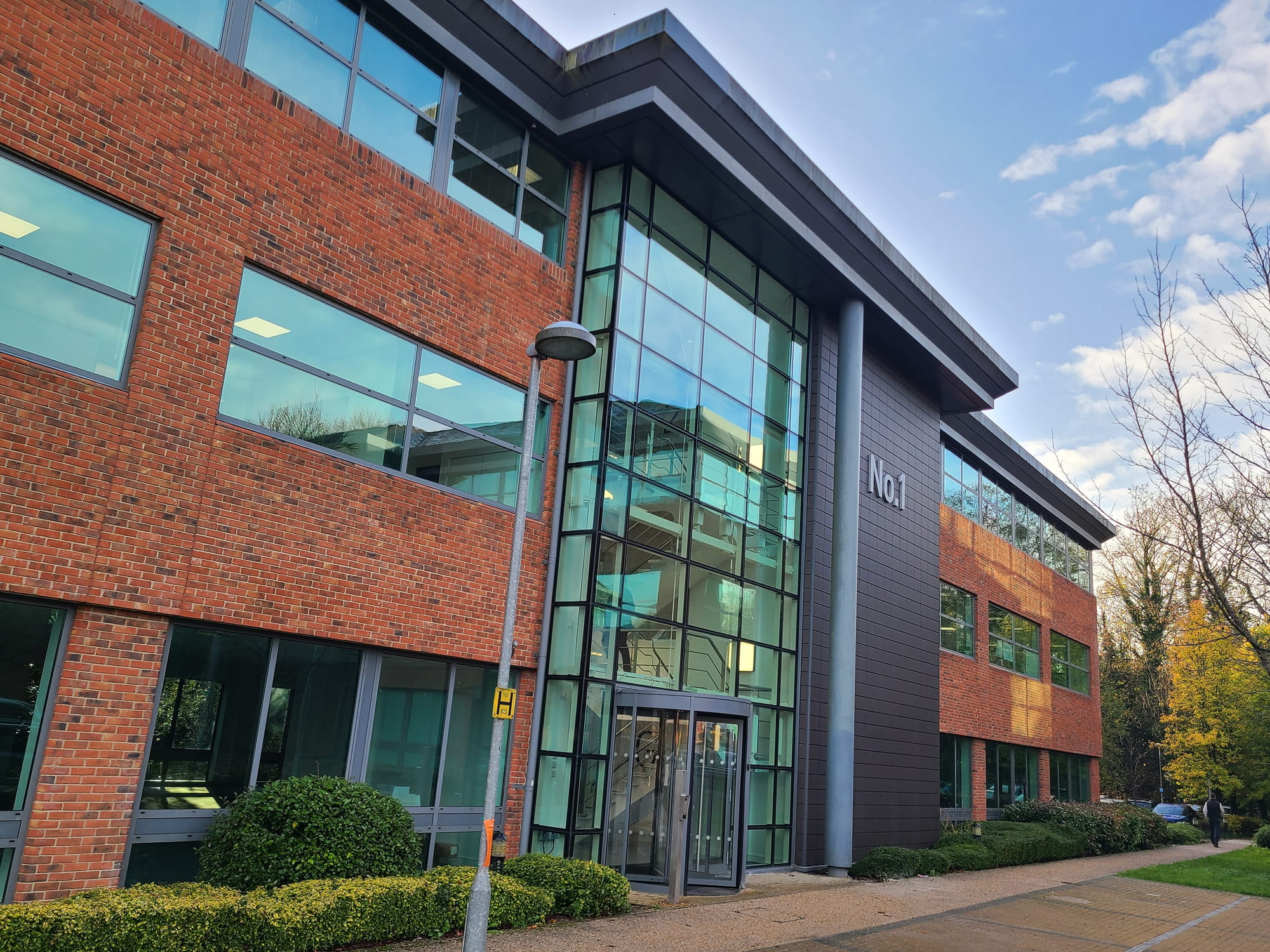Modern brick building with large glass windows, labeled "No.1," surrounded by greenery and a pathway.