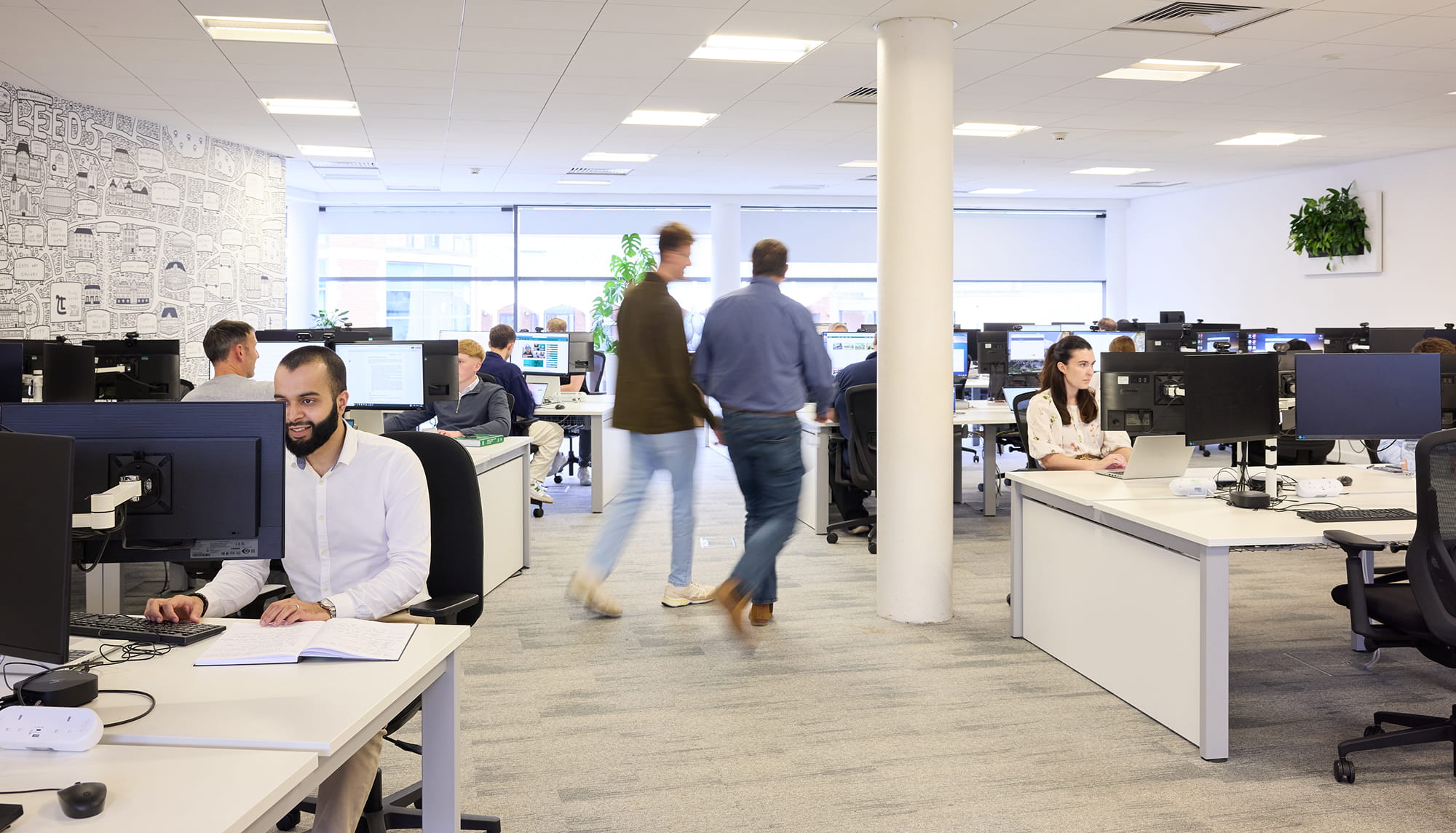 Modern office space in Leeds with employees working at desks, some using computers while others walk between workstations.