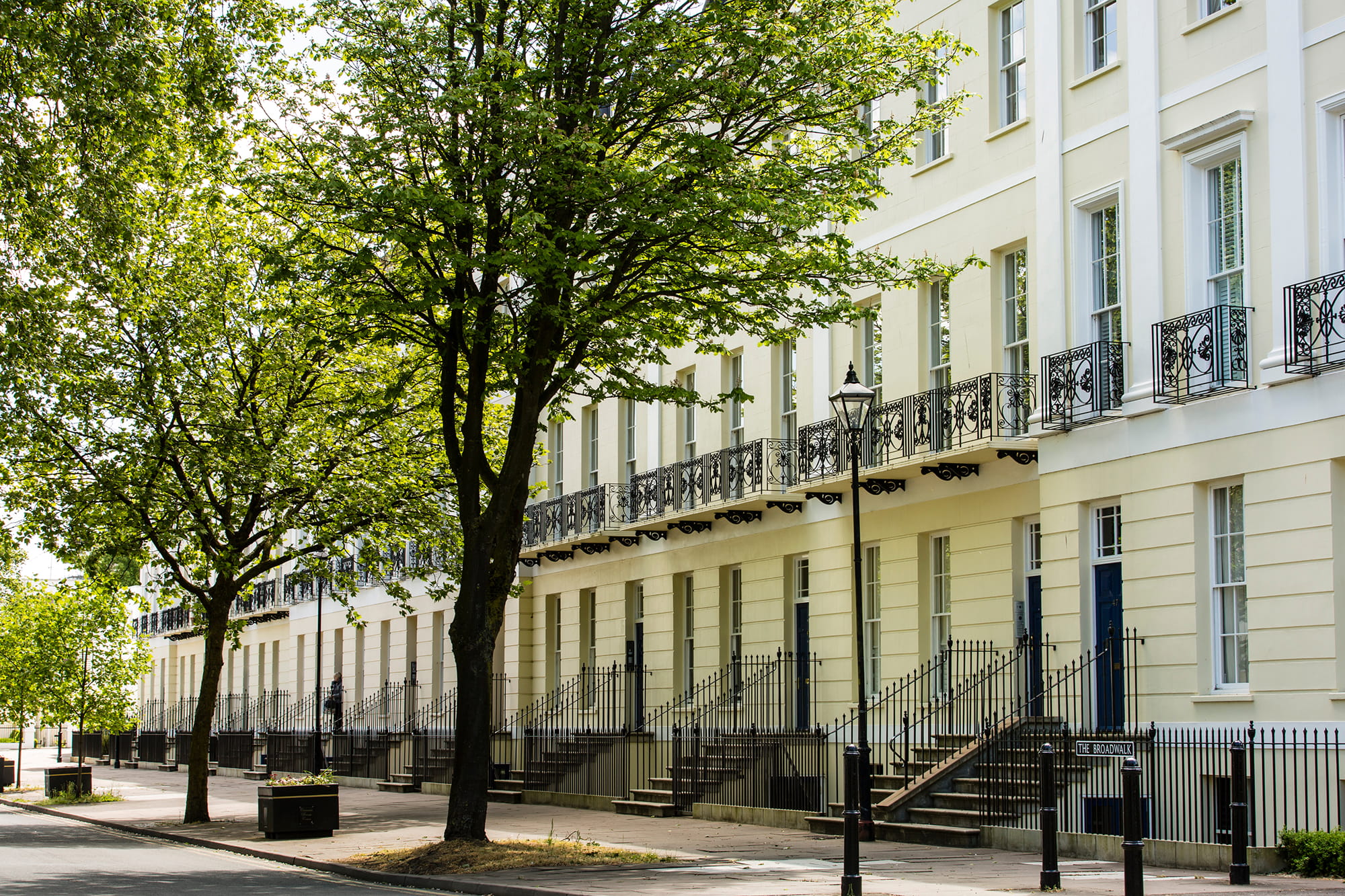 Row of elegant white townhouses with wrought iron balconies, lined by trees and street lamps.