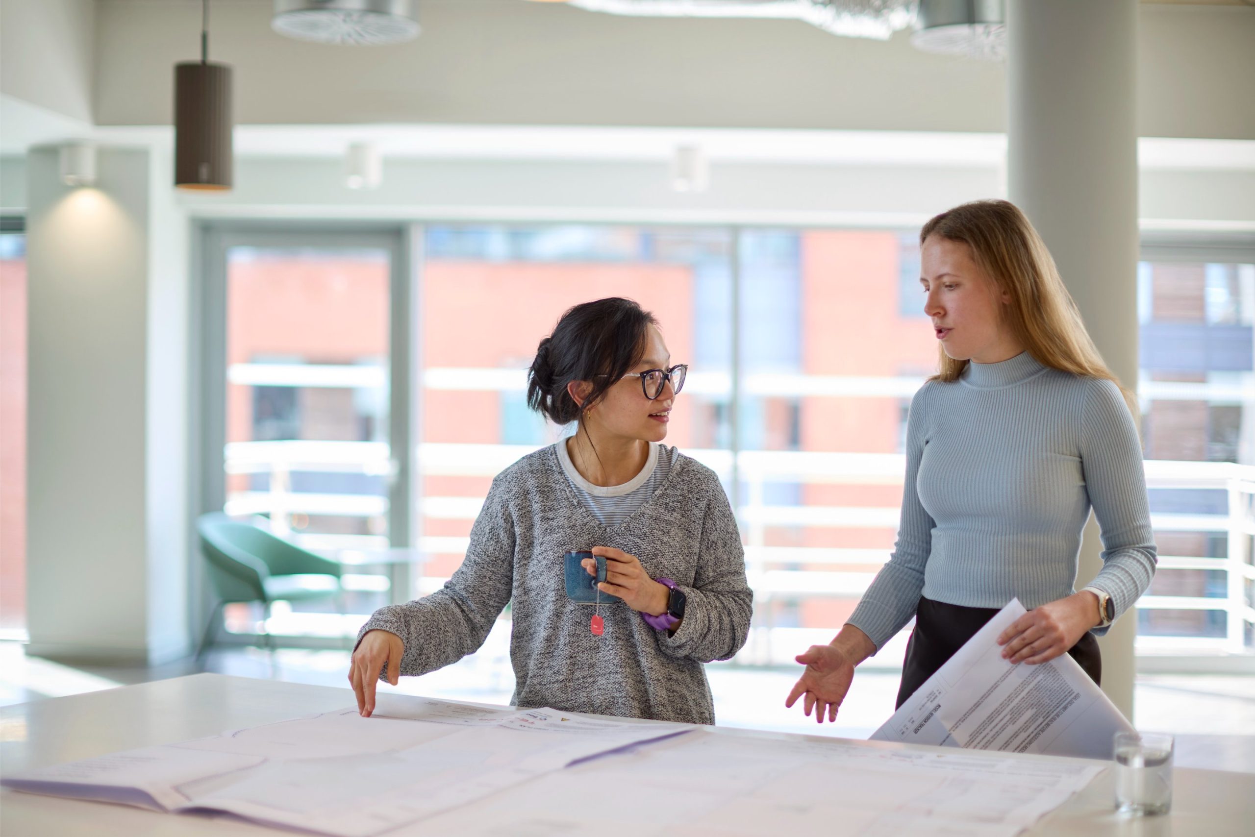 Two women discussing architectural plans at a table in a bright, modern office space.